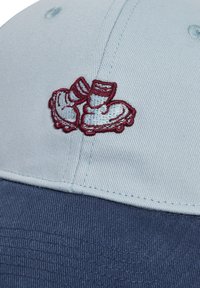 Keps med ljusblå ovandel och mörkblå skärm, med broderade röda rullskridskor framtill. Tyget har en strukturerad yta.