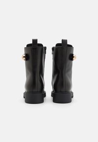 Stivali ankle in pelle nera con un design elegante, punte arrotondate, zip laterali e evidenti accenti in metallo dorato a forma di cerchio.