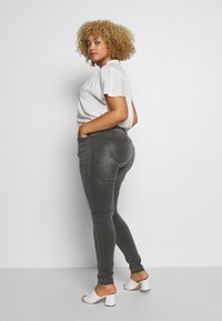 Gray skinny jeans with a high waist, featuring a smooth texture and two back pockets, paired with a white short-sleeve top and white heeled mules.
