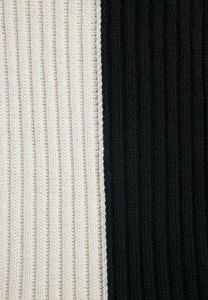 Stickad tyg i vertikala ränder, uppdelad i kontrasterande sektioner av vitt och svart. Varje sida har texturerad detalj med snygg sömnad.