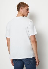 White short-sleeve t-shirt with a round neckline, smooth texture, and relaxed fit, worn with dark blue jeans. No visible patterns or logos.