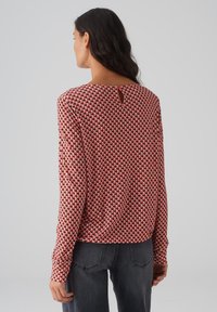 Langärmlige Bluse mit rot-weißer Musterung und einem Schlüsselloch-Detail am Rücken, aus weichem Stoff und mit lockerer Passform.