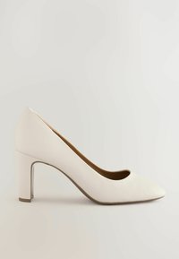 Zapato de tacón alto blanco hecho de cuero texturizado, con punta redondeada, superficie lisa y un robusto tacón cuadrado para mayor soporte.