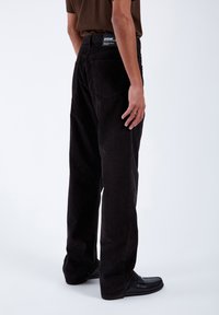 Black corduroy pants with a straight-leg cut, featuring two back pockets, and a fabric label on the waistband. Textured, soft material.