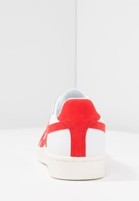 Vita sneakers med röda mockadetaljer och sömmar. Rund häl, låg design och en strukturerad gummisula för bra grepp.
