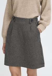 Sort-hvid ternet nederdel med plisseringer, der har en talje med to sorte knapper. Fremstillet af et struktureret stof.