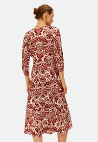 Jurk tot op de knie met een crèmekleurige basis en ingewikkeld maroon bloemenpatroon, met driekwartmouwen en een knoopsluiting met sleutelgAT-achterdetail.