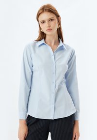 Camicia azzurra chiaro con maniche lunghe, colletto a punta e vestibilità aderente. Texture liscia con delicati dettagli delle cuciture.