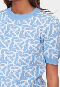 Světle modrý krátký svetr s krátkým rukávem, zdobený bílým abstraktním vzorem, s žebrovaným kulatým výstřihem a mírně nabíranými rukávy.