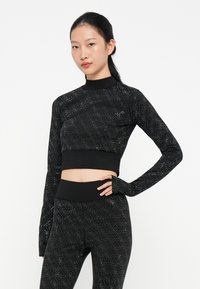 Top atletico nero corto con maniche lunghe, caratterizzato da un motivo a diamante testurizzato e accenti riflettenti. Abbinato a leggings a vita alta coordinati.