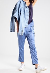 Jeansjacka i ljusblått, i kombination med en mörkblå tanktop och ljusblå byxor med knytning i midjan. Vita sneakers fulländar outfiten.