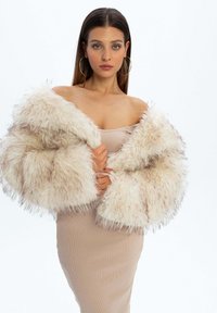 Kurtka z faux futra w kolorze kremowym, o puszystej fakturze i oversize'owym kroju. Minimalistyczny styl, połączona z dopasowaną, jasnobeżową sukienką.