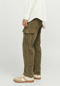 Olive green corduroy cargo pants with multiple pockets, straight leg design, and textured fabric. Paired with beige sneakers featuring brown accents.