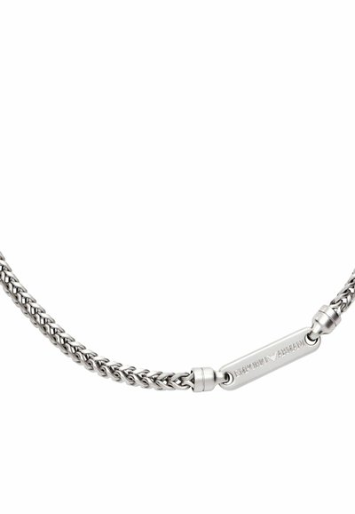 Stříbrný náramek s řetízkovým vzorem, plochá visačka s vyrytým logem a zaoblené spojky na zapínání.