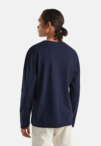 Granatowa koszula z długim rękawem, okrągłym dekoltem, luźnym fasonie i miękkiej teksturze. Gładka tkanina bez widocznych wzorów i akcentów.