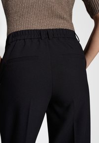 Black elastic-waist pants, featuring two back pockets, a smooth texture, and a tailored fit. Fabric has a slight sheen.