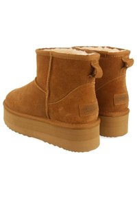 Botas de tobillo de ante marrón con forro interior suave, suelas planas y tiradores en la parte posterior. Punta redondeada y un mínimo de costuras.