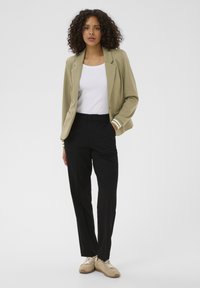 Light olive green blazer with white striped cuffs, white top, black trousers, and beige sneakers; smooth fabric, tailored fit, modern design.