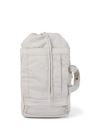 Cream-colored drawstring backpack with front pockets, two round buttons, side handle, and zipper compartment at the bottom.