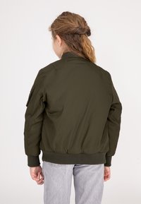 Olijfgroene bomberjack met ribgebreide manchetten en onderrand, met een zijzak. Glad textuur, aansluitend ontwerp en lichtgewicht materiaal.