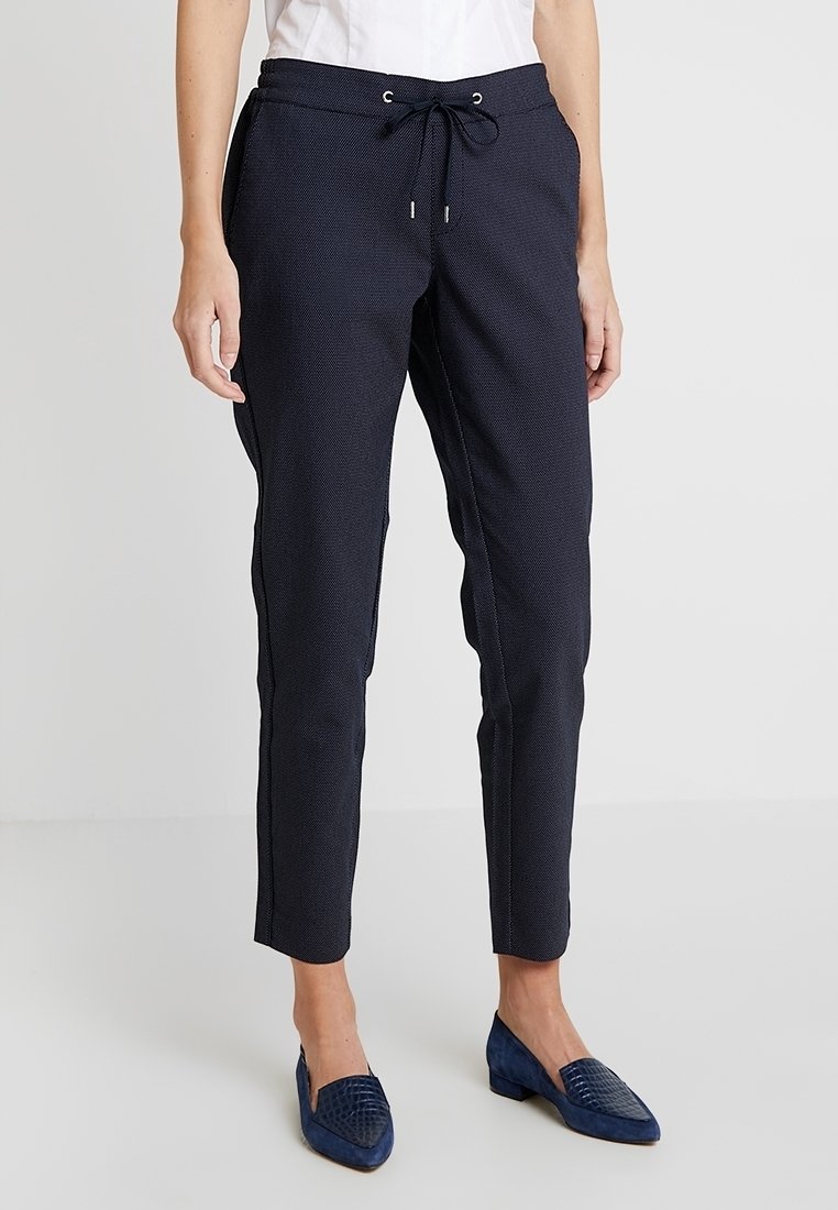 Pantalons de survêtement navy avec un tissu texturé et une coupe tapered, dotés de œillets métalliques et d'accents latéraux contrastés. Associés à des chaussures navy.