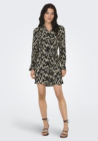 Μαύρο και μπεζ φόρεμα με σχέδιο, με ζώνη στη μέση, μακριά μανίκια και γιακά. Το ύφασμα έχει απαλή υφή με αφηρημένο σχέδιο ζιγκ-ζαγκ.