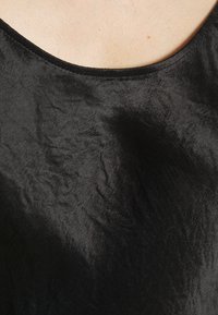 Gros plan d'un haut en tissu noir froissé avec un décolleté arrondi sur un fond de peau claire.