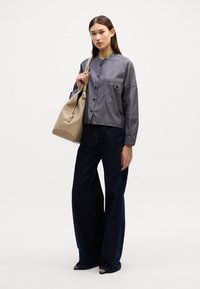 Gestreept grijs overhemd met een patch pocket, gecombineerd met donkere wijde jeans en een beige leren schoudertas met een gesp.