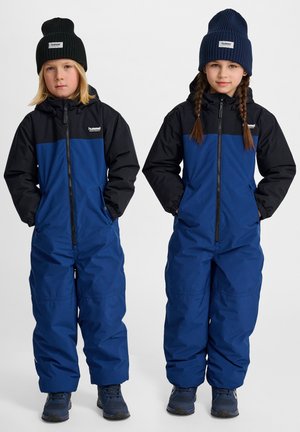 Blauwe en zwarte geïsoleerde sneeuwpakken met ritssluitingen, elastische manchetten en zijzakken. Gebreide mutsen in donker groen en marineblauw.