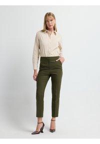 Beige overhemd met knopen en een kraag, gecombineerd met hoogopstaande olijfgroene tapse broek en puntige bruine hakken.