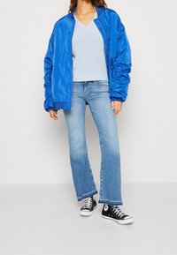 Blå blanka bomberjacka, ljusblå stickad topp, urtvättade blå vida jeans och svarta högskor med vita detaljer.