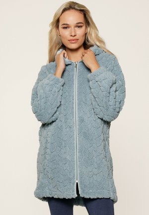 Lichtblauwe, fluffy jas met een gestructureerd, schubachtig design. Voorzien van een rits aan de voorkant en een gezellige capuchon. Lange, oversized mouwen.