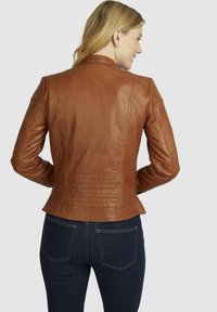 Chaqueta de cuero marrón con un diseño ajustado, costuras visibles y detalles acolchados en la parte posterior. Usada sobre unos jeans oscuros.
