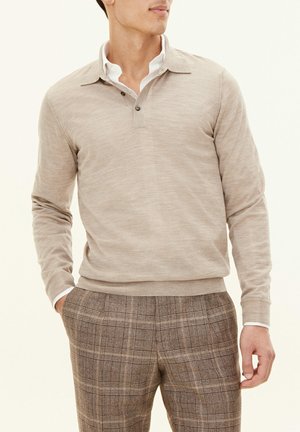 Beige strikket pullover med krave, to-knaps front og ribbede manchetter; sat sammen med brune ternede skræddersyede bukser.