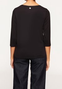 Černý top s dlouhými rukávy a kulatým výstřihem, se třičtvrtinovými rukávy. Na zadní straně má malý kovový detail. Měkký a hladký materiál.