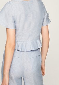 Helles blaues Leinenoberteil mit kurzen, ausgestellten Ärmeln und einem Peplum-Saum. Es zeichnet sich durch eine glatte Textur und ein schlichtes Design aus.