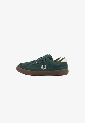 Zapatilla deportiva de ante verde oscuro con suela marrón, logo de laurel blanco en el lateral y tira en el talón color crema, vista desde el lado exterior.