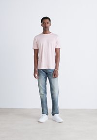 Ljusrosa T-shirt med kort ärm, denimjeans i en blekt blå nyans och vita sneakers. Enkelt mönster med avslappnad passform och mjuk textur.