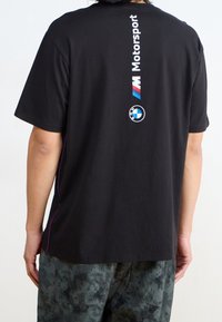 Mustapaitaa lyhyellä hihalla, jossa selässä "Motorsport" -teksti ja BMW-logo valkoisena ja sinisenä. Sivusaumoissa on purppurat yksityiskohdat.