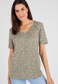 Camisa de manga corta y escote en V de tela verde con un patrón variado de manchas blancas y naranjas. Corte sencillo y relajado con una textura suave.