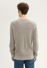 Hellbrauner Strickpullover mit strukturiertem Finish, runden Ausschnitt und langen Ärmeln. Kombiniert mit blauen Jeans.