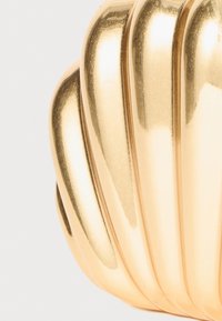 Gold-toned decorative object with a ribbed design and smooth texture, resembling a shell shape with a reflective surface.