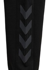 Pantalones deportivos negros que presentan una textura de tela suave, adornados con patrones de chevron verticales en un acabado mate a lo largo de los lados.