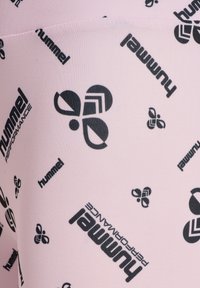 Różowe elastyczne legginsy z powtarzającym się czarnym wzorem logo z napisem "hummel" oraz różnymi kształtami geometrycznymi. Gładka tekstura.