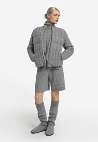 Ensemble tricoté gris comprenant une veste matelassée zippée, un short assorti et des chaussettes hautes décontractées avec des poignets côtelés.