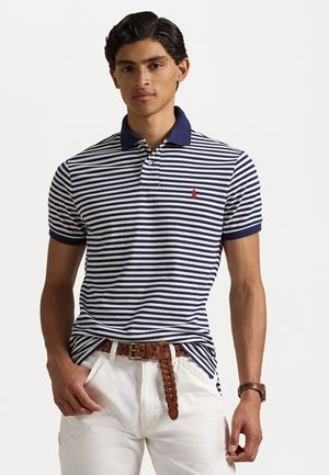 Navy- og hvitstripet polo skjorte med solid navy krage, som har en liten rød logo. Båret med hvite bukser og et flettet brunt lærbelte.