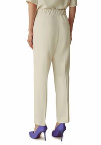 Pantaloni di colore crema con elastico in vita e design a gamba dritta. Presentano una tasca posteriore, abbinati a scarpe col tacco alto di colore viola.