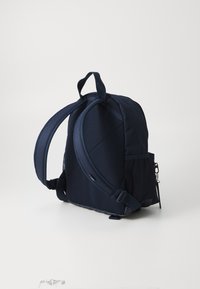 Mørkeblå ryggsekk med polstrede skulderstropper, teksturert stoff, en mesh-lommepocket på siden, og en liten glidelåsdetalj foran.
