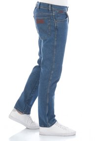 Jeans in denim blu con taglio dritto, design standard a cinque tasche e patch in pelle sulla tasca posteriore. Indossati con sneakers bianche.