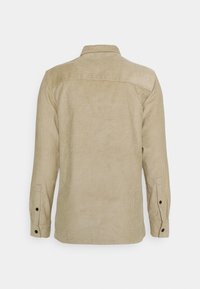 Beżowa koszula ze sztruksu z długimi rękawami, mankietami na guziki, kołnierzykiem i lekko teksturowaną powierzchnią z pionowymi prążkami na całej powierzchni.